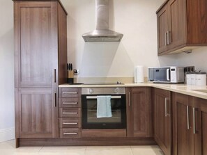 A kitchen with wooden cabinets, a stainless steel range hood, an oven, a microwave, and a countertop with a kettle and a toaster.