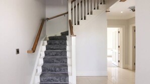 Un escalier avec des rampes blanches et des mains courantes en bois, menant à un palier.