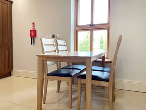 A dining area with a wooden table and chairs, a window with natural light, and a fire alarm on the wall.