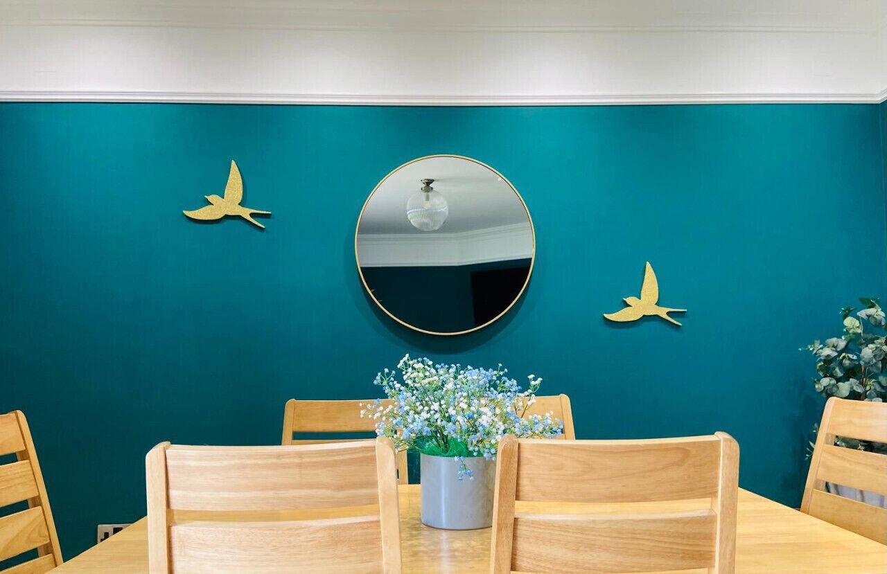 Un coin repas avec des murs de couleur turquoise, un miroir rond et deux décorations représentant des oiseaux dorés.