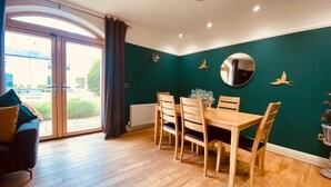 Un comedor con una mesa y sillas de madera, un espejo grande y vistas al exterior a través de un ventanal.