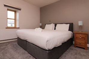 A bedroom with a large bed, a nightstand, a lamp, and a window.