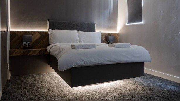 A modern bedroom with a large bed, bedside lamps, and a small window.
