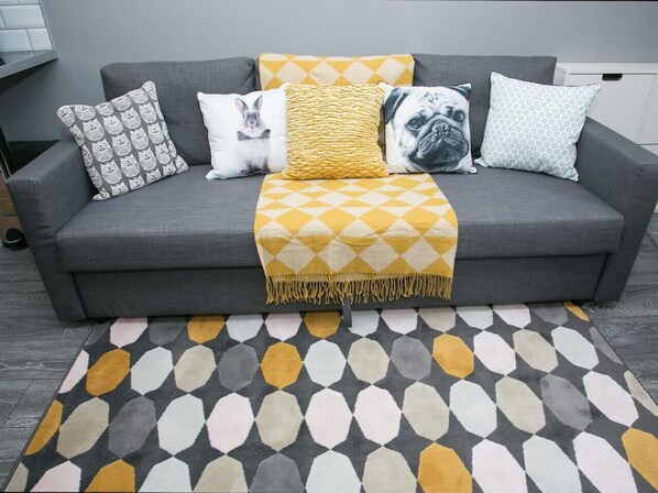 A grey sofa with a yellow throw blanket, patterned pillows, and a geometric rug.