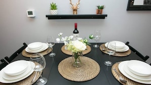 A dining table set with white plates, cutlery, and wine glasses, centered with a vase of flowers.
