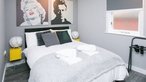 A modern bedroom with a bed, pillows, a nightstand, and artwork on the wall.