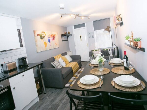 Un espacio habitable compacto con kitchenette, comedor y sofá con cojines.