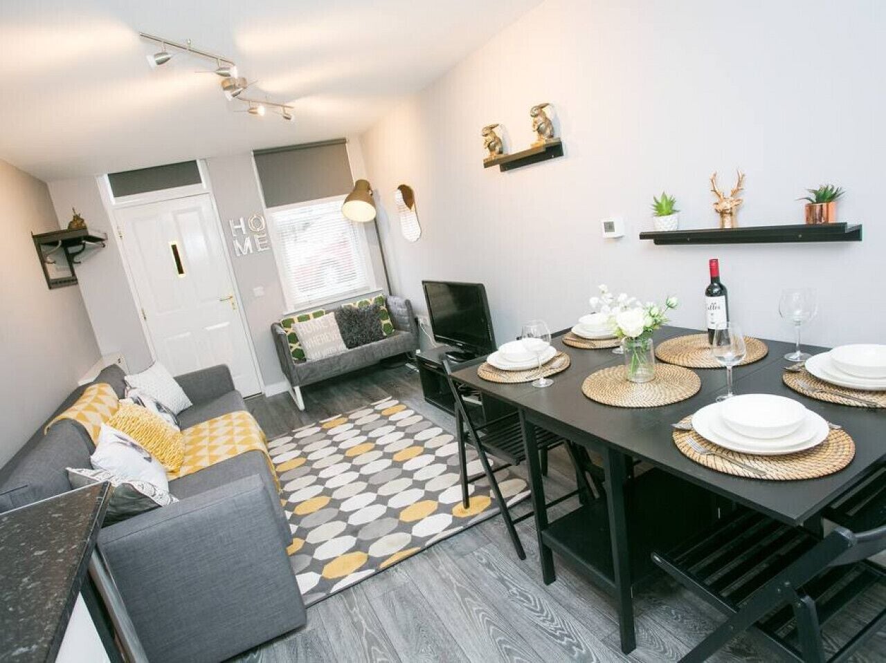 A modern living room with a sofa, a dining table set for four, and a TV.