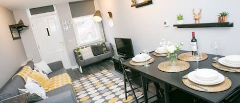 Una sala moderna con un sofá, una mesa de comedor preparada para cuatro personas y un televisor.