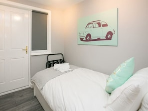 Un dormitorio con una cama, una ventana, una puerta e ilustración de un coche colgada en la pared.