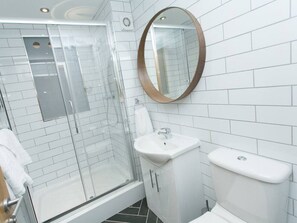 Moderni kylpyhuone, jossa on lasiseinällä varustettu suihku, valkoinen pesuallas ja wc.