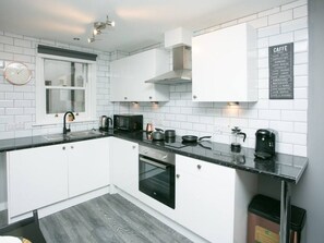 Una cocina moderna con armarios blancos, encimeras negras, horno integrado, microondas y cafetera.