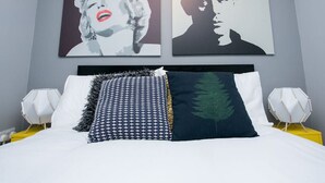 Una cama con almohadas estampadas, una almohada verde oscuro con forma de hoja y un cabecero de diseño geométrico.