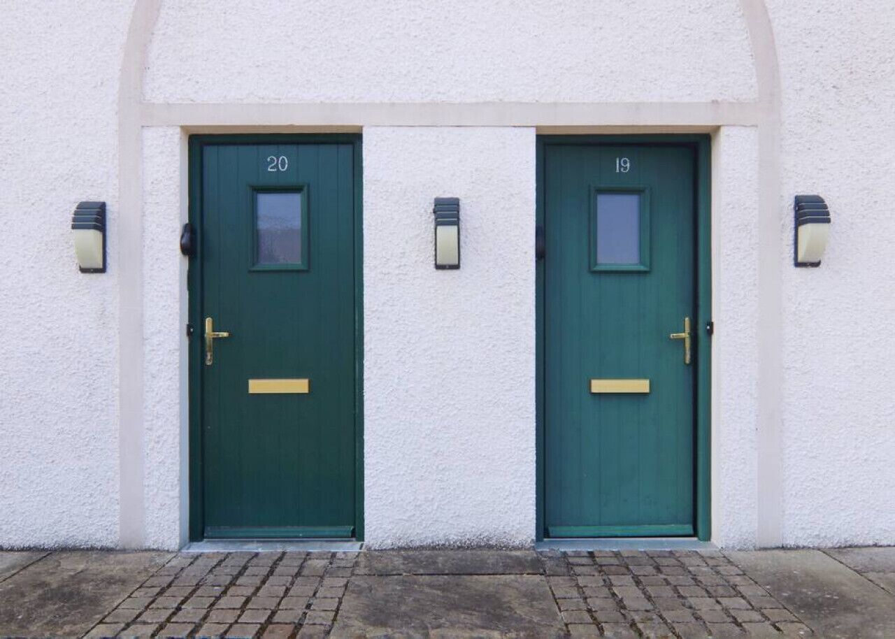 Two green doors with numbers 20 and 19, white textured walls, and small wall-mounted lights.