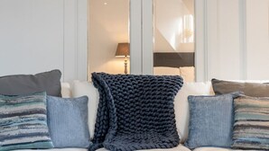 Un salon comprenant un canapé, deux tables d’appoint et une grande fenêtre donnant sur une lampe et un lit.