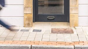 Une porte noire, dotée d’une poignée en laiton et d’un panneau de verre, est encadrée dans une façade en pierre surmontée d’une arche décorative.