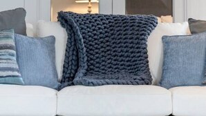 Un canapé blanc agrémenté d’un plaid tricoté bleu foncé et de coussins assortis.