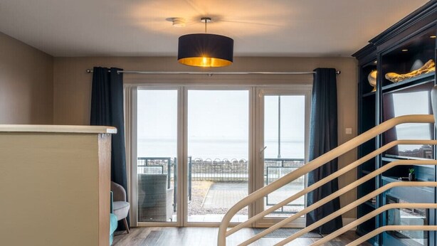 Habitación de hotel con puerta corrediza de vidrio que da a un balcón, una escalera y un ventanal con vistas al mar.