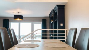 Un comedor moderno con una mesa larga, sillas con cojines y una escalera que sube a un nivel superior.