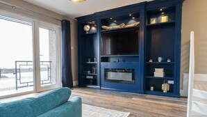Una sala de estar moderna con un ventanal grande, un sofá azul, una chimenea y estanterías empotradas.
