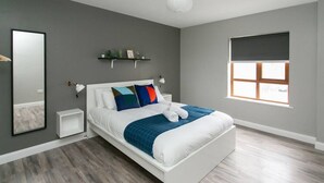 A modern bedroom with a white bed, grey walls, a large window, and a small shelf with decorative items. - University Road 1 · Spacious & Modern + Central Location|Couples Break (Belfast)
