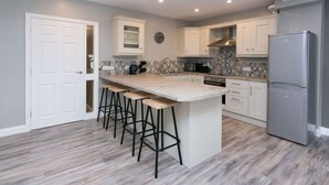 A modern kitchen with a central island, bar stools, a refrigerator, and a clock on the wall. - University Road 1 · Spacious & Modern + Central Location|Couples Break (Belfast)