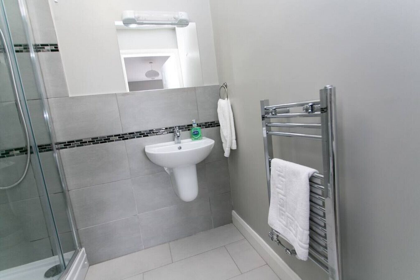 Un baño con cabina de ducha de vidrio, un lavabo blanco y un perchero para toallas.