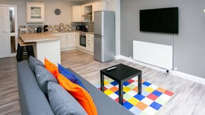 A modern kitchen with a refrigerator, stove, and microwave. There is a dining area with a table and chairs. A flat-screen TV is mounted on the wall. - University Road 1 · Spacious & Modern + Central Location|Couples Break (Belfast)