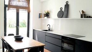 A modern kitchen with a wooden dining table, black chairs, a black countertop, and a hanging light fixture. - Maison de Ville à Proximité du Port et des Commerces! (Camaret-sur-Mer)