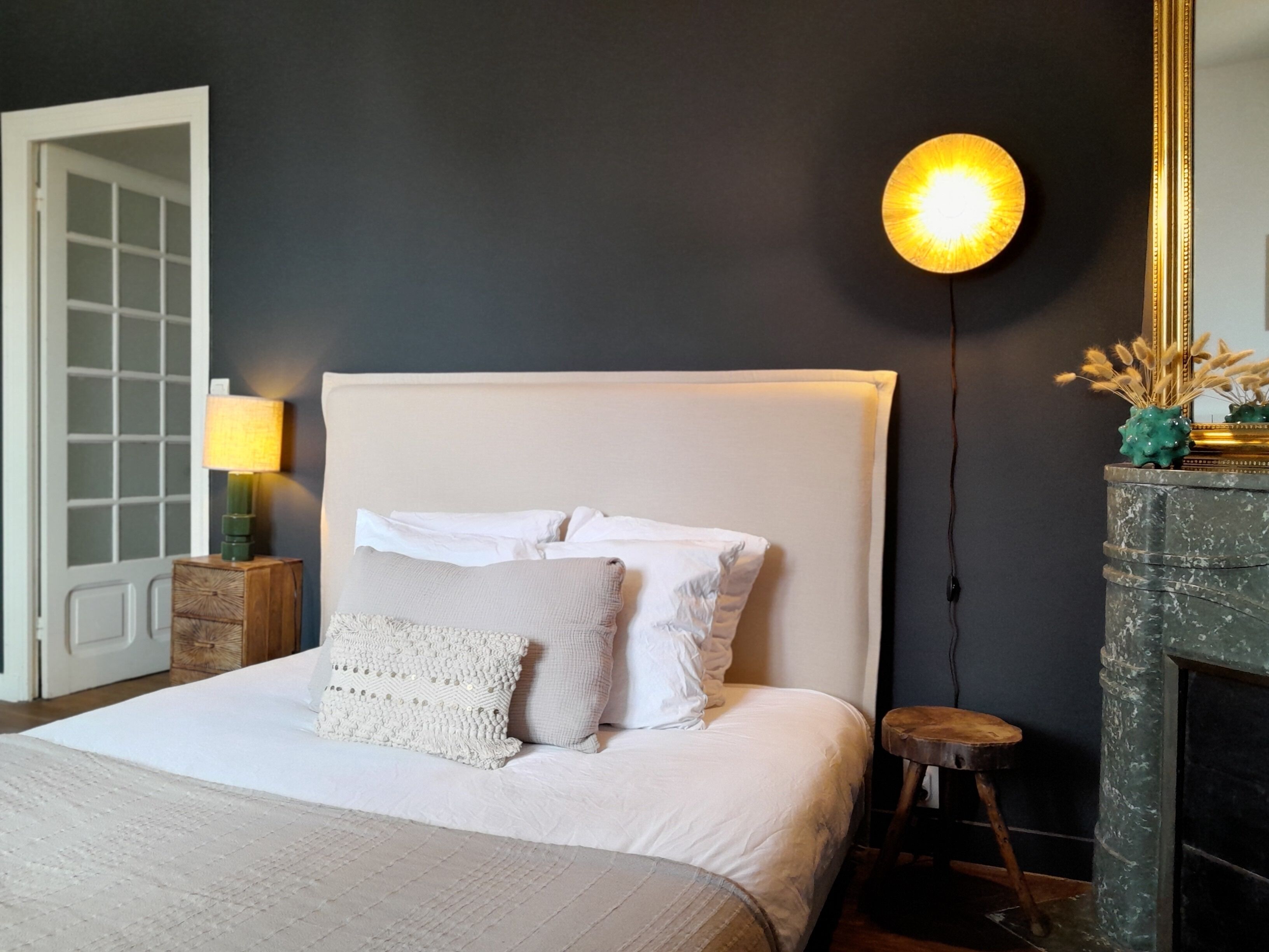Une chambre à coucher avec un grand lit, une table de chevet avec une lampe, un luminaire fixé au mur et une cheminée.