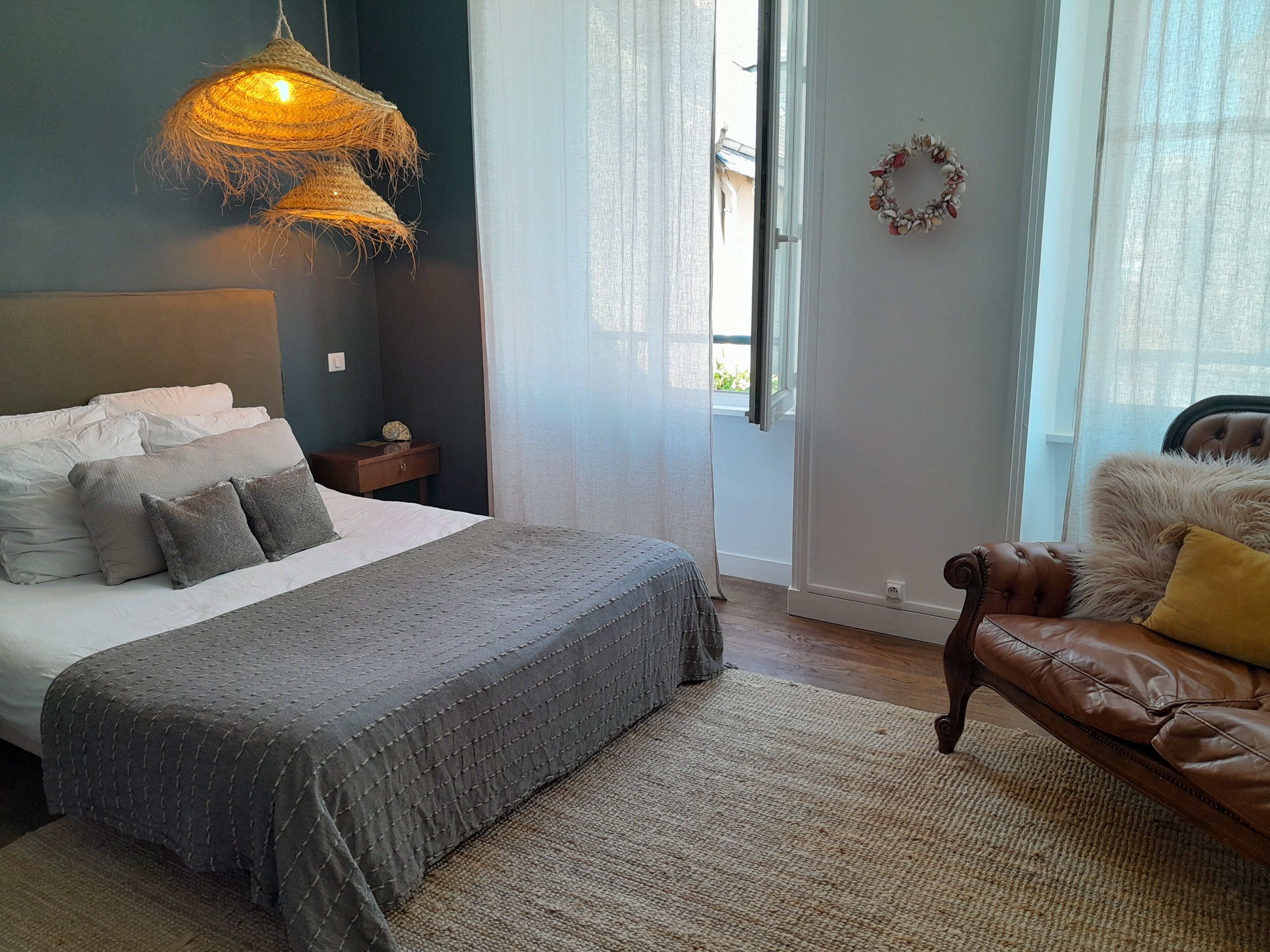 A bedroom with a large bed, a leather sofa, a hanging light fixture, and a window with curtains.