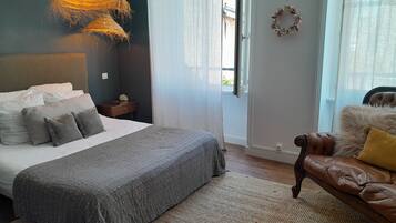 A bedroom with a large bed, a leather sofa, a hanging light fixture, and a window with curtains.