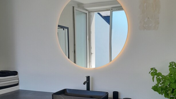 A modern bathroom with a round mirror, black sink, and four woven baskets on a dark countertop. - Maison de Ville à Proximité du Port et des Commerces! (Camaret-sur-Mer)