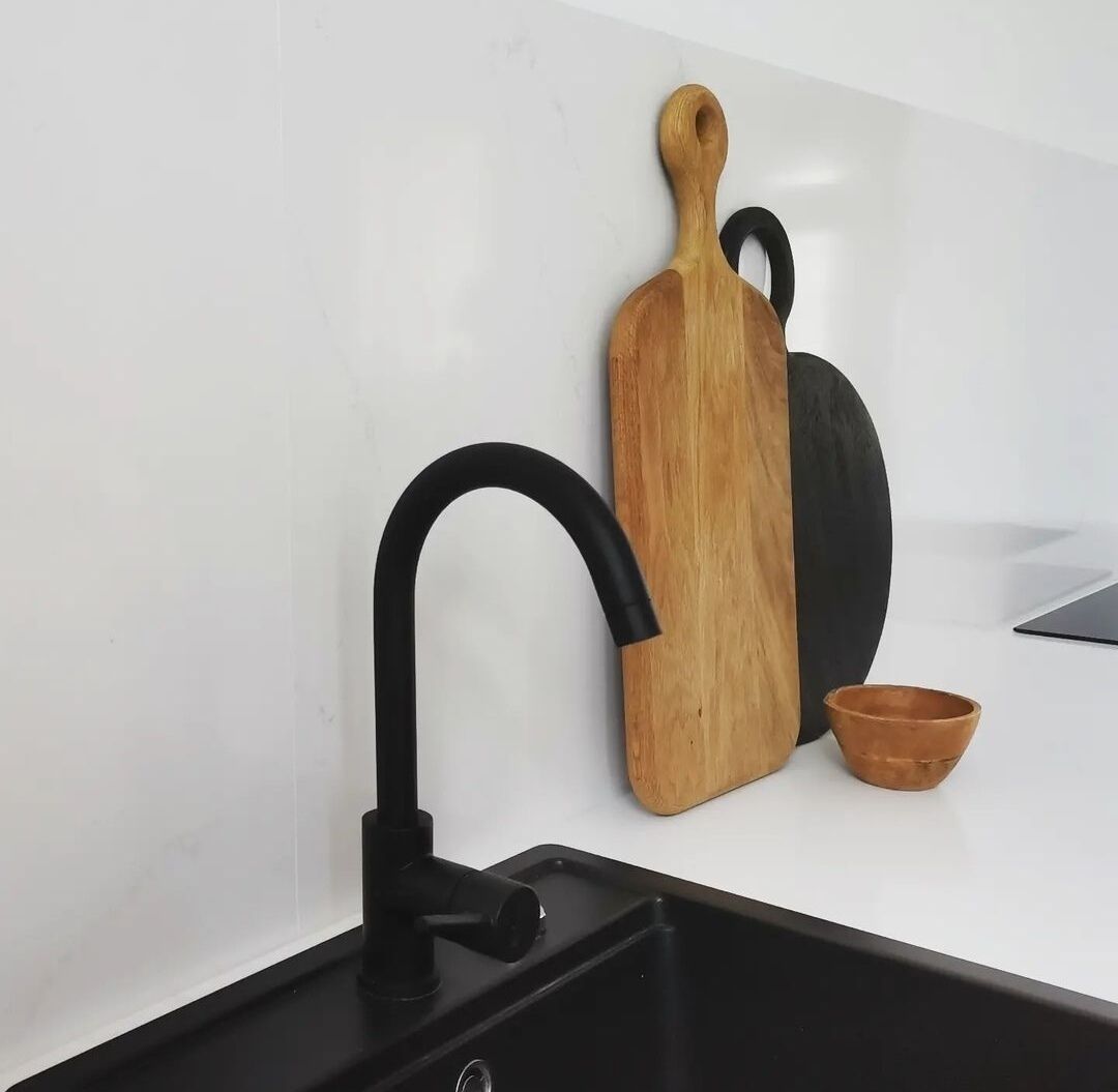 Une cuisine avec un robinet noir, une planche à découper en bois et un petit bol marron.
