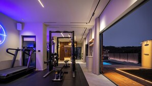 Un gimnasio moderno en casa con equipo de ejercicio, un ventanal y vista a una piscina.