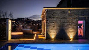 Un área de piscina moderna al aire libre con un jacuzzi climatizado, un manantial termal y vistas a un pueblo en la colina al atardecer.