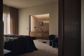 A bedroom with a bed, a wooden wardrobe, a desk with a lamp, and a chair.