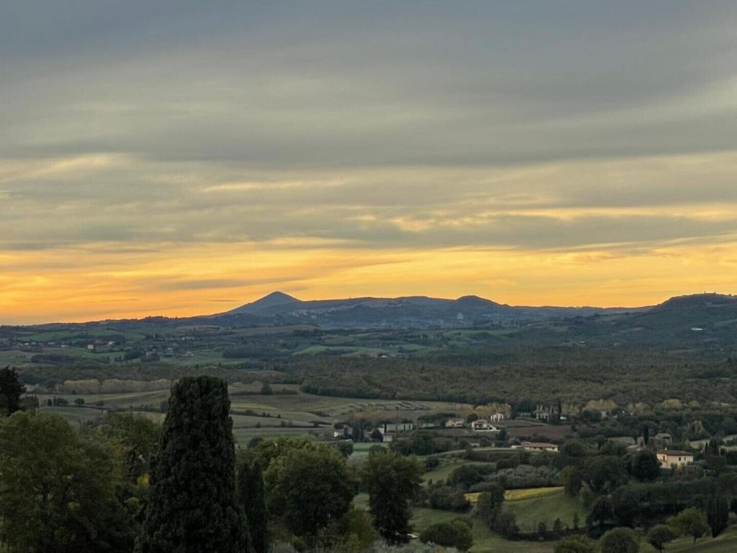 A panoramic view of a rural landscape with rolling hills, a prominent mountain in the distance, and scattered buildings.