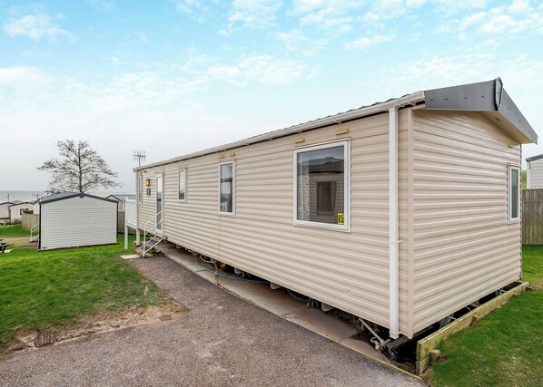 A single-story mobile home with a front porch, a small attached garage, and a clear sky.