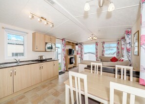 A modern kitchen with a microwave, toaster, and sink. There is a dining area with a table and chairs, and a sofa with red cushions. - Otterton Premier Plus 2 (Budleigh Salterton)