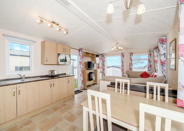 A modern kitchen with a microwave, toaster, and sink. There is a dining area with a table and chairs, and a sofa with red cushions.