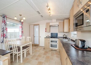 A compact kitchen with a dining area, a microwave, a toaster, and a stove. - Otterton Premier Plus 2 (Budleigh Salterton)
