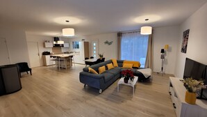 A modern living room with a sofa, coffee table, and a dining area with chairs and a table. - Maison Neuve Bord de Dordogne (Lanzac)