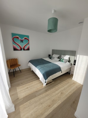 A modern bedroom with a bed, a chair, a painting, and a ceiling light.