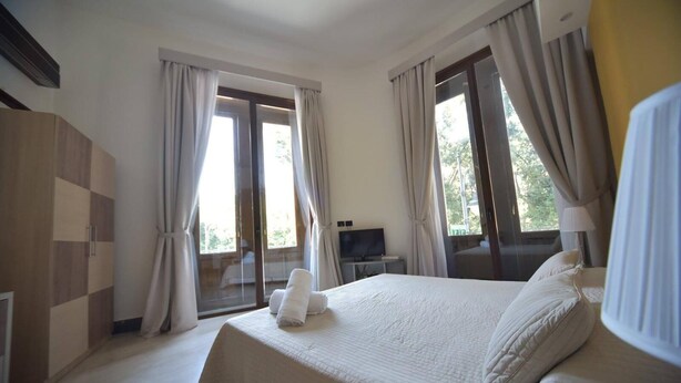 A hotel room with a large bed, a TV on a side table, and a balcony with curtains. - Duomo156 (Messina)