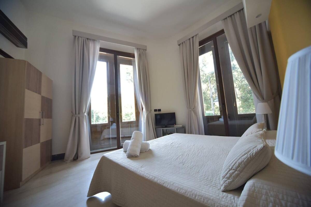 A hotel room with a large bed, a TV on a side table, and a balcony with curtains.