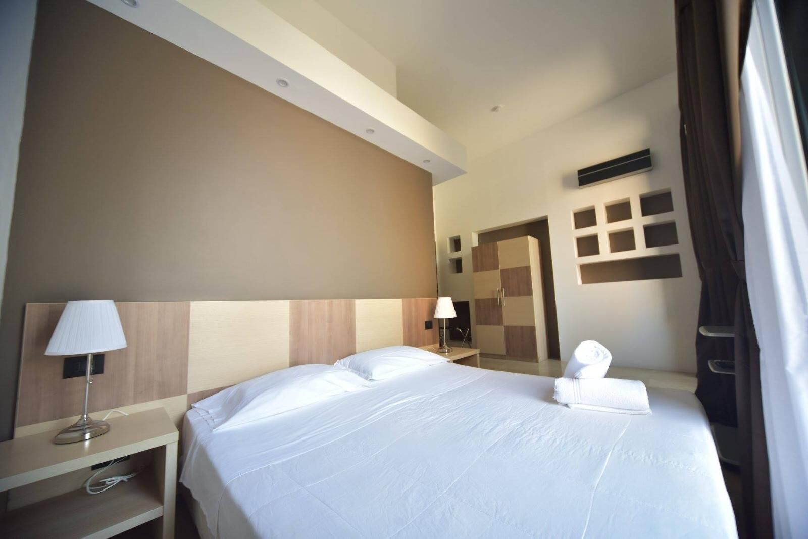 Una habitación de hotel con una cama grande, una mesita de noche, una lámpara, un armario y un espejo.