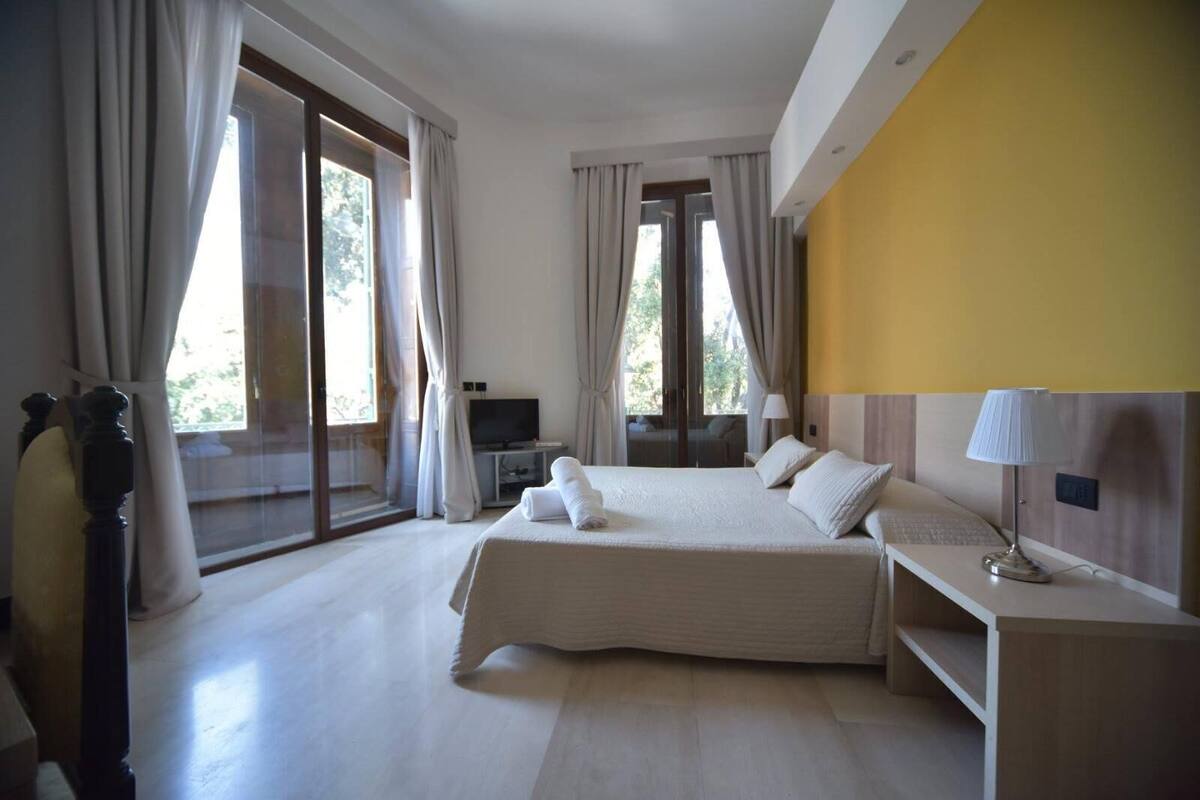 A bedroom with a large bed, a TV, and a desk with a lamp.