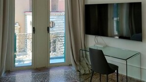 A room with a glass door leading to a balcony, a flat-screen TV mounted on the wall, and a glass table with a chair. - Duomo156 (Messina)