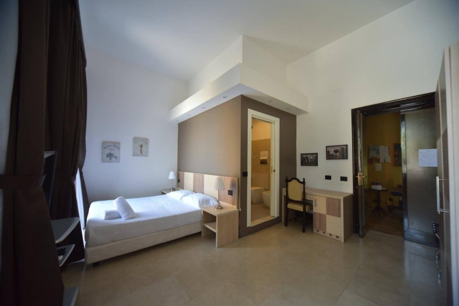 Habitación de hotel con cama, escritorio, silla, espejo y puerta que da a un baño.